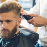 Young man sitting in a barbershop while barber trimming the hair
